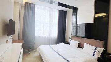 A hotel room with a large bed, a desk, a television, and a window with curtains.