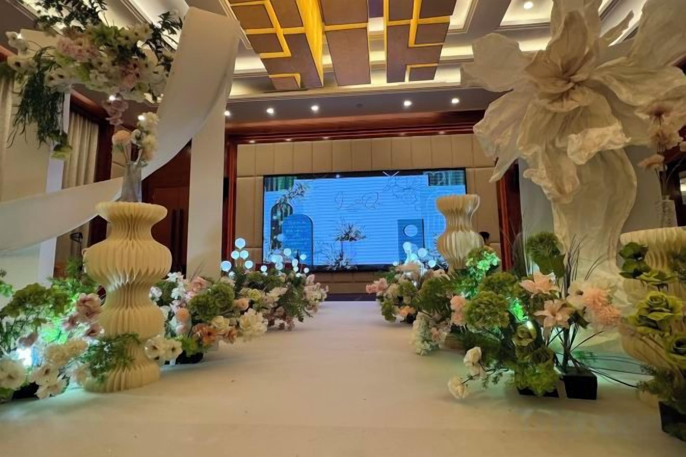 Un vestíbulo de hotel con un escenario central, jarrones decorativos y arreglos florales.