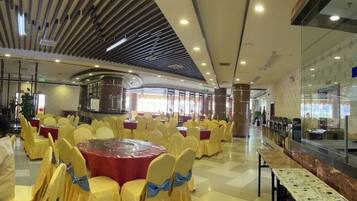 A banquet hall with round tables and chairs, a central stage, and a glass wall with a view.