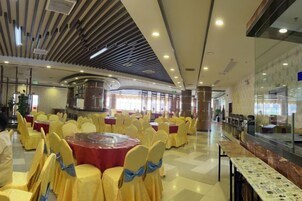 Un salón de banquetes con mesas redondas y sillas, un escenario central y un muro de cristal con vistas.
