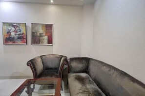 Una sala de estar con un sofá, un sillón y una mesa de centro. Hay dos cuadros abstractos en la pared.