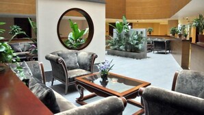 A lobby with grey upholstered sofas, a round mirror, and a coffee table with a vase of flowers. - Lifeng Hotel (Zhaoping)
