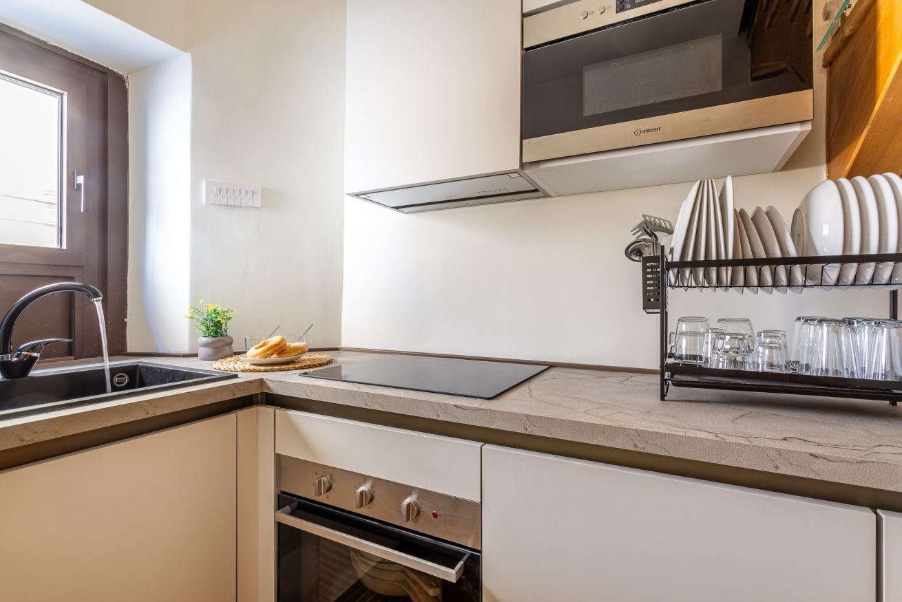 A kitchen with a built-in oven, a dishwasher, and a dish rack with glasses.