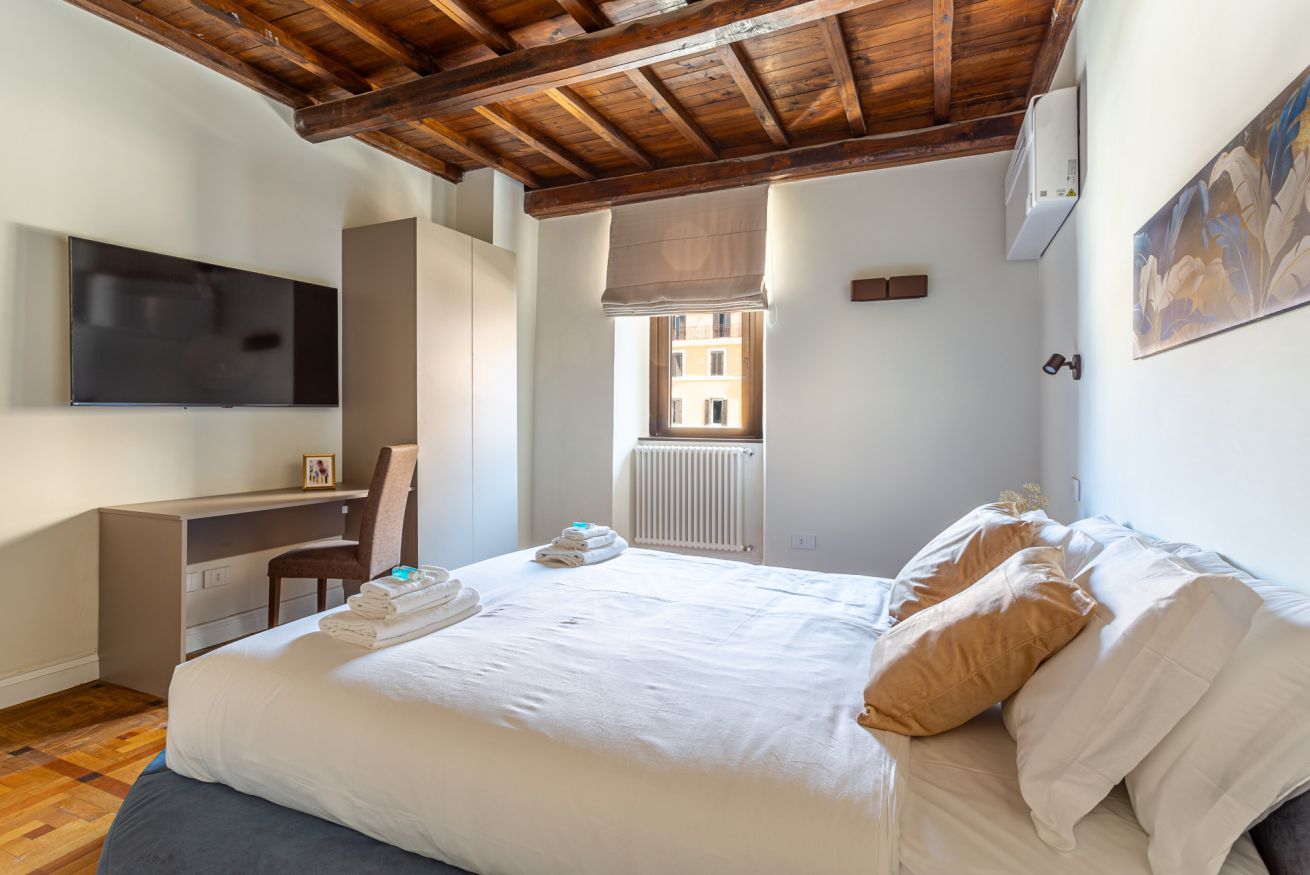 A bedroom with a bed, a desk, a chair, a television, a window, and a radiator.