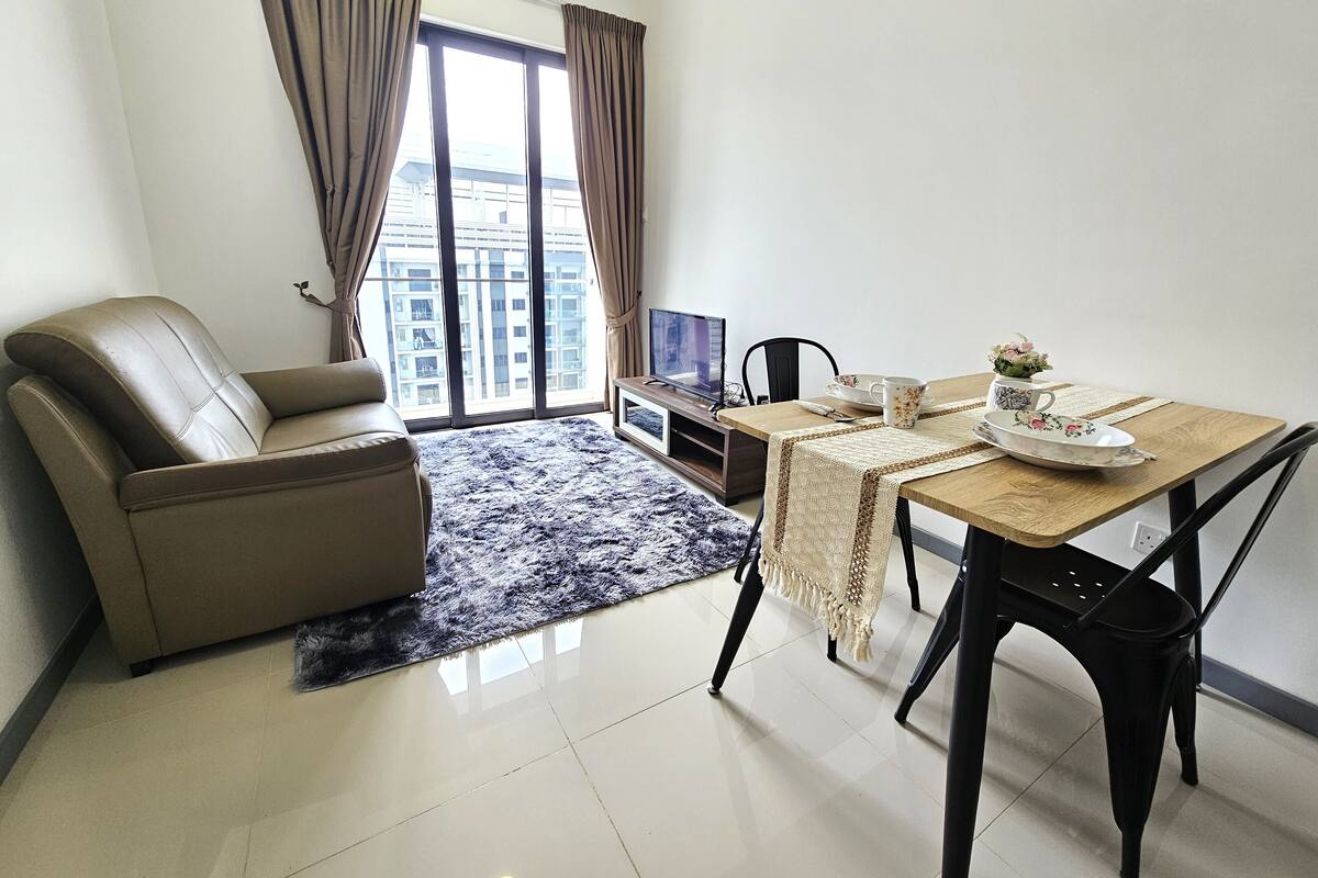 Una sala de estar moderna con un sofá de cuero, una mesa de comedor con sillas, un televisor y vistas a un paisaje urbano a través de amplios ventanales.