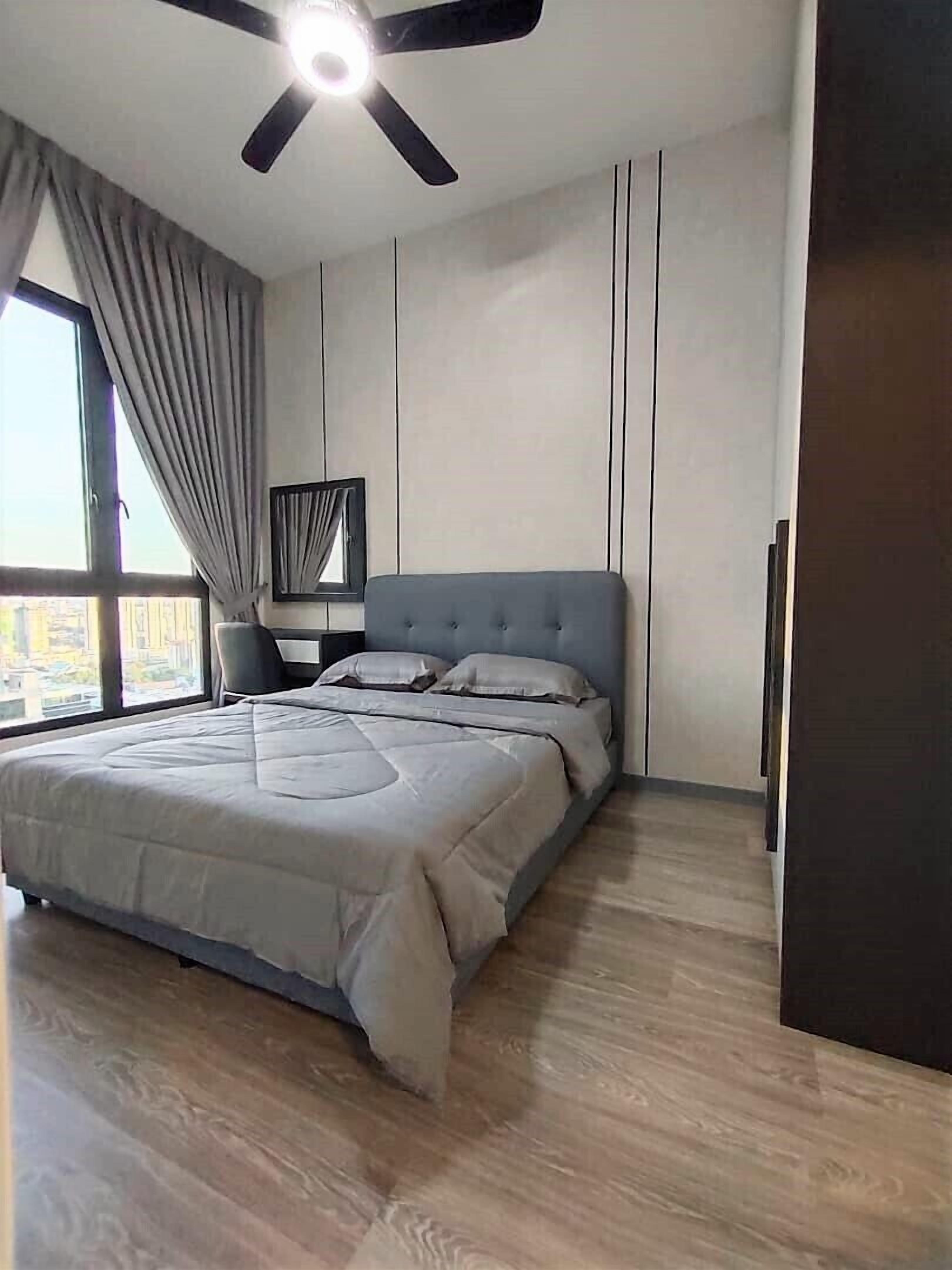 A bedroom with a large bed, a ceiling fan, a nightstand, and a window with curtains.