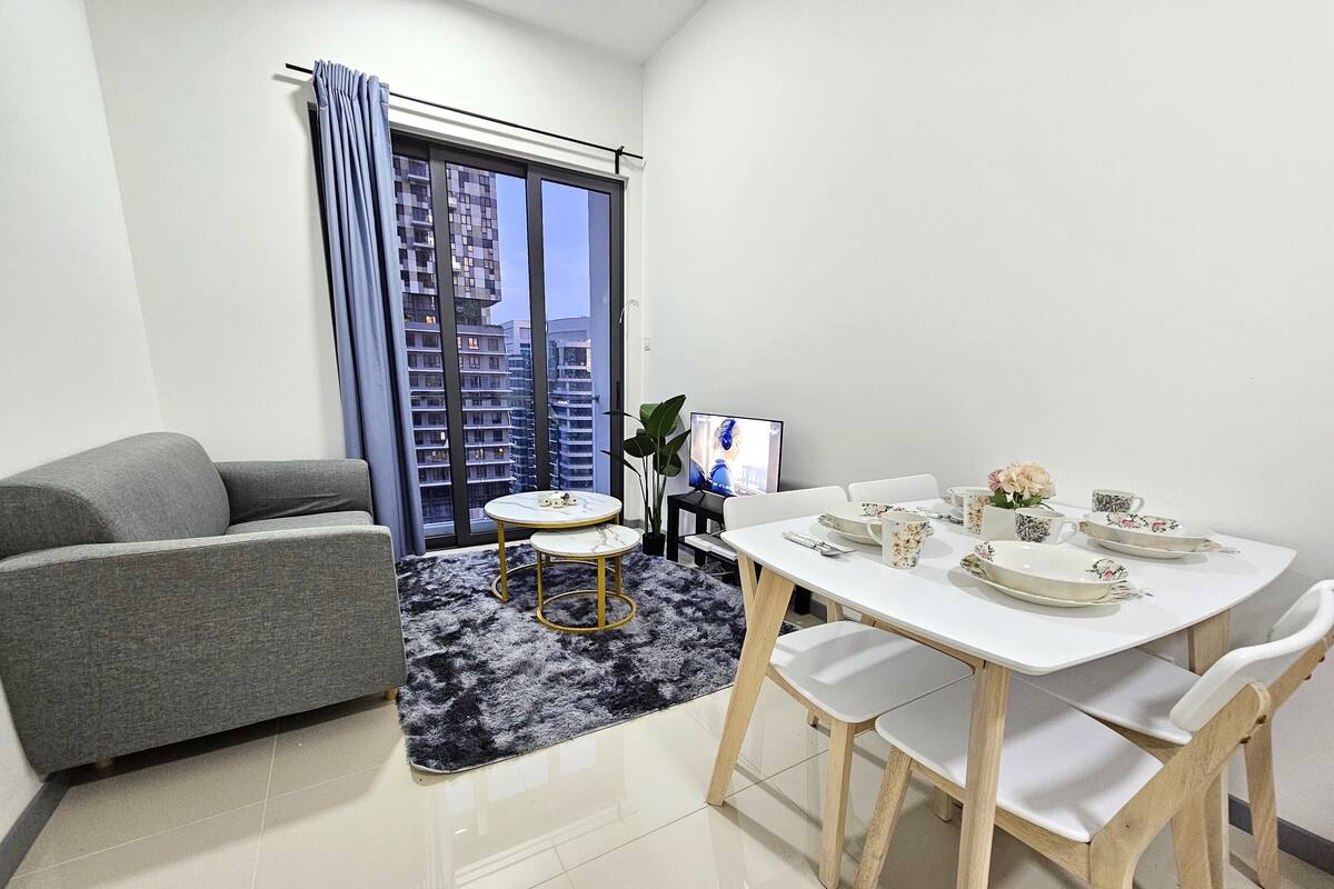 Una sala moderna con un sofá gris, una mesita redonda y una mesa de comedor con platos y tazas blancos.