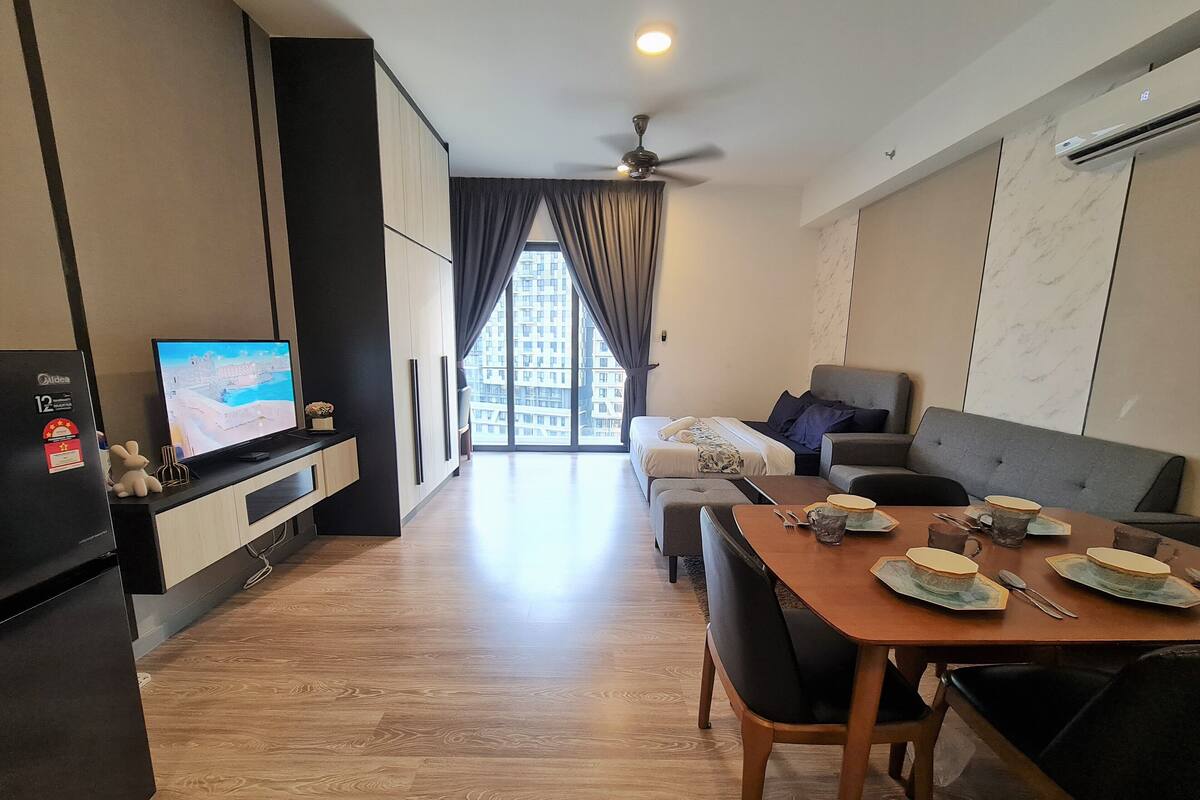 Una habitación de hotel moderna con zona de comedor, sofá, cama y televisor.