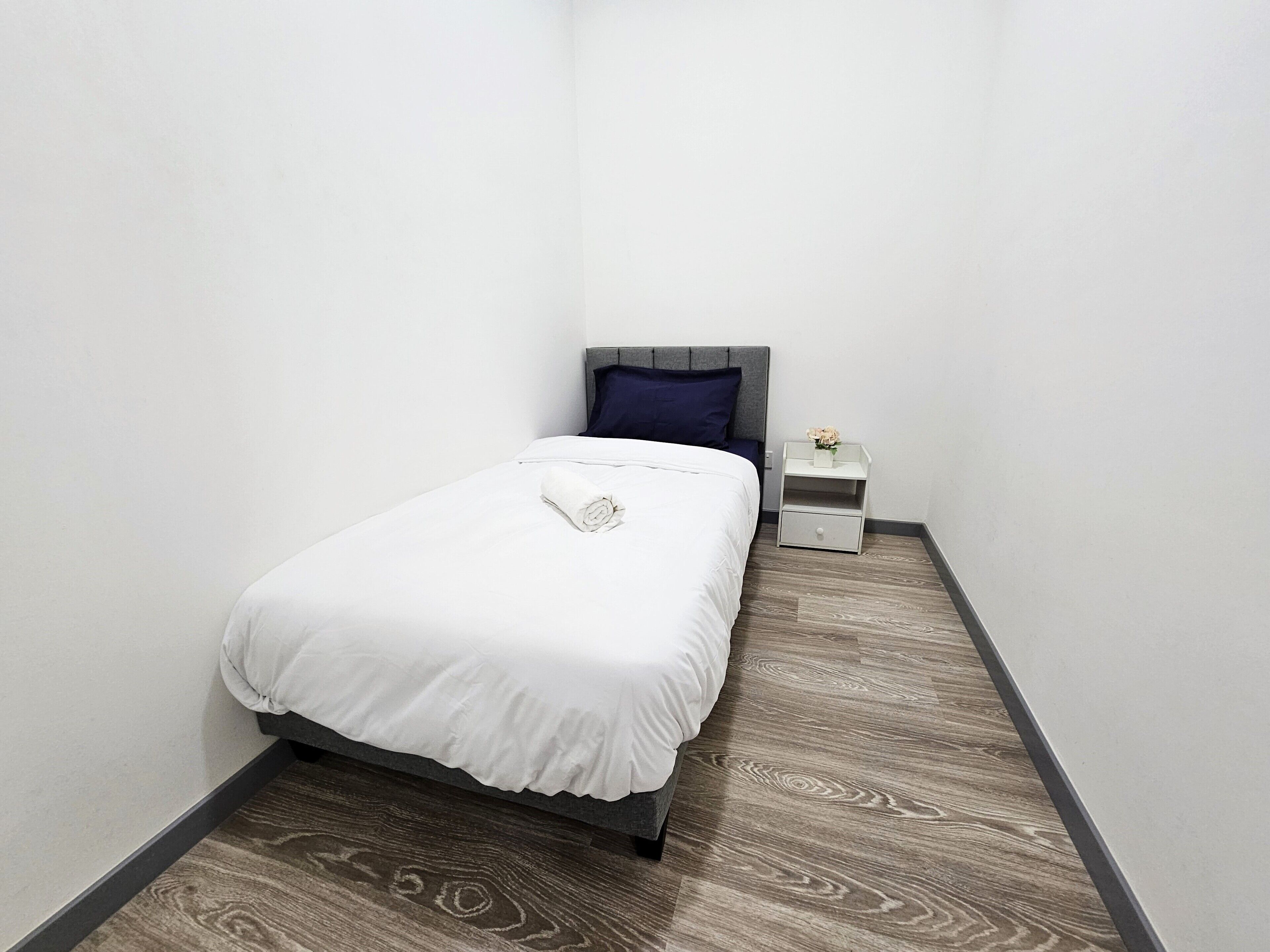 Une petite chambre à coucher, bien rangée, avec un lit, une table de chevet et une étagère fixée au mur.