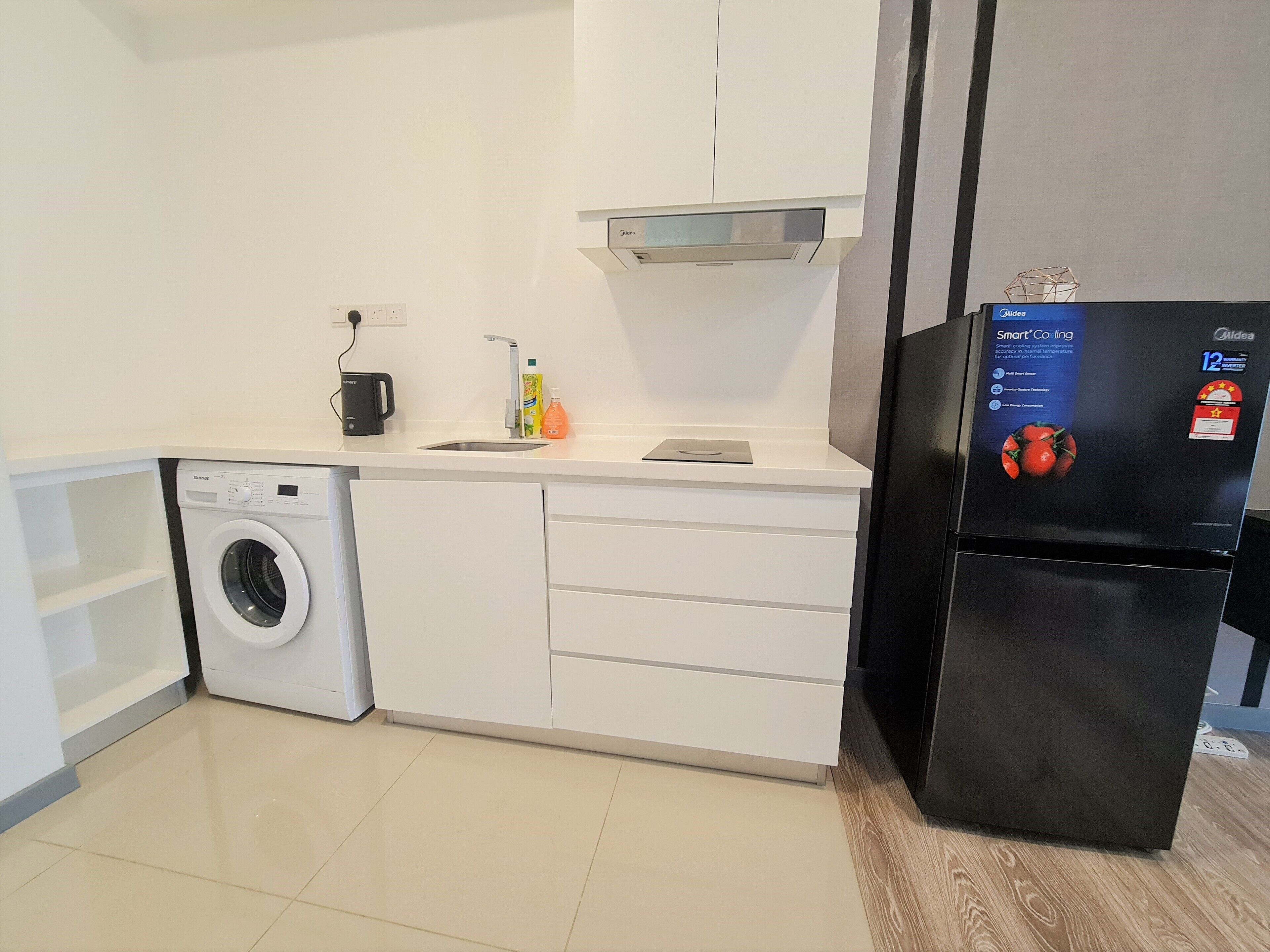 Eine kleine Küche mit Waschmaschine, einem schwarzen Kühlschrank und einem Spülbecken mit Armatur.