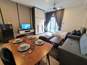 Una habitación de hotel moderna con zona de comedor, sofá, televisor y balcón con vistas.