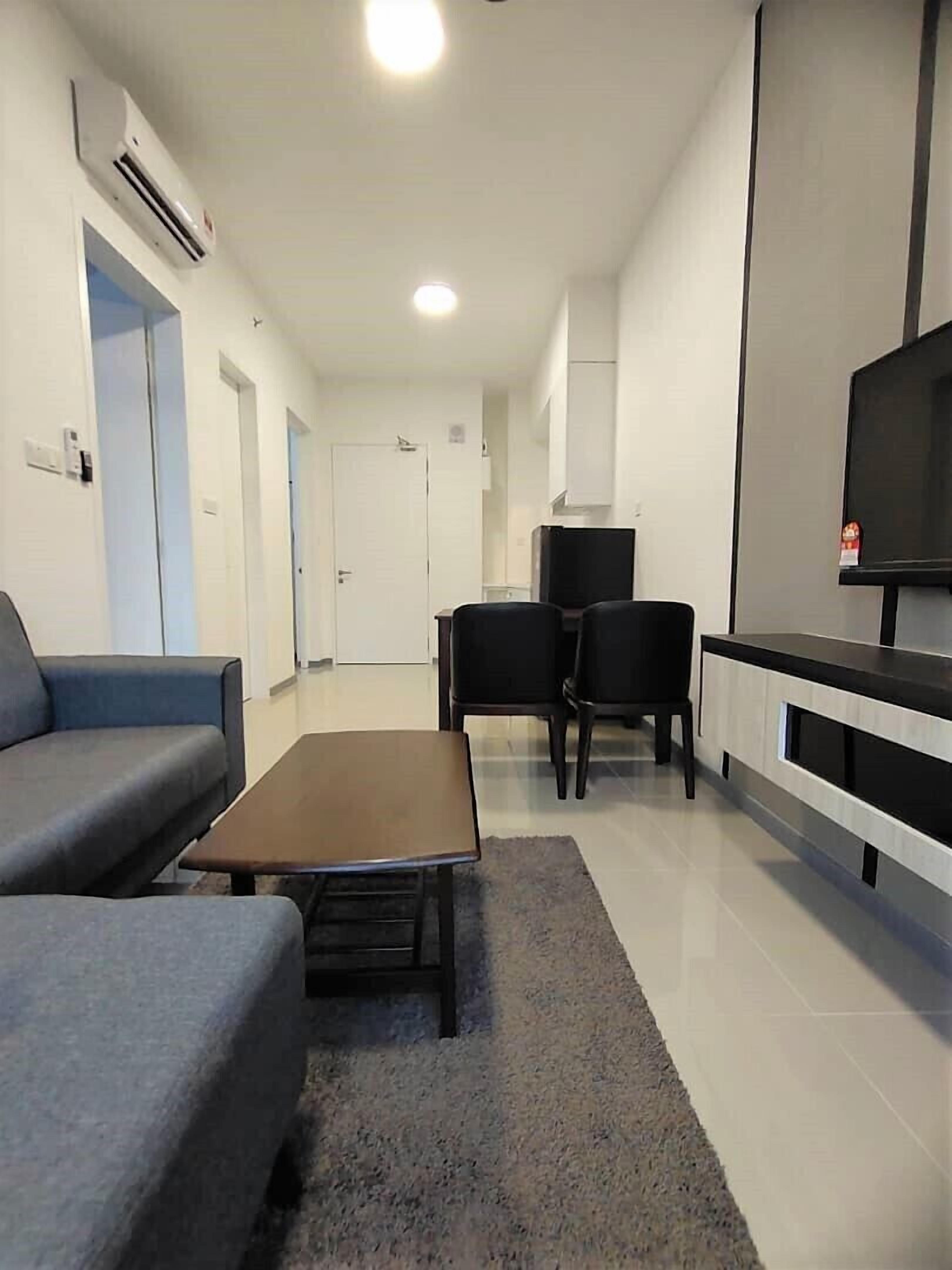 A modern living room with a sofa, a coffee table, and a TV. There are two chairs and a small table in the dining area.
