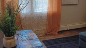 Olohuoneessa on sohva, sohvapöytä, jossa on kaukosäädin, ruukkukasvi ja seinällä taulu.