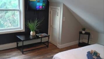 Un dormitorio con una cama, un televisor montado en la pared, una ventana y una mesita con una planta.