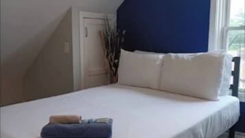 Une chambre avec un grand lit, du linge de lit blanc, un coussin bleu en guise d’élément décoratif, et une fenêtre donnant sur un beau paysage.