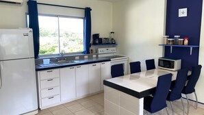 Een kleine keuken met een koelkast, fornuis, magnetron en een eethoek met stoelen.