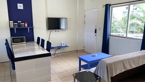 Een kleine kamer met een bed, een tafeltje, een televisie en een kitchenette.