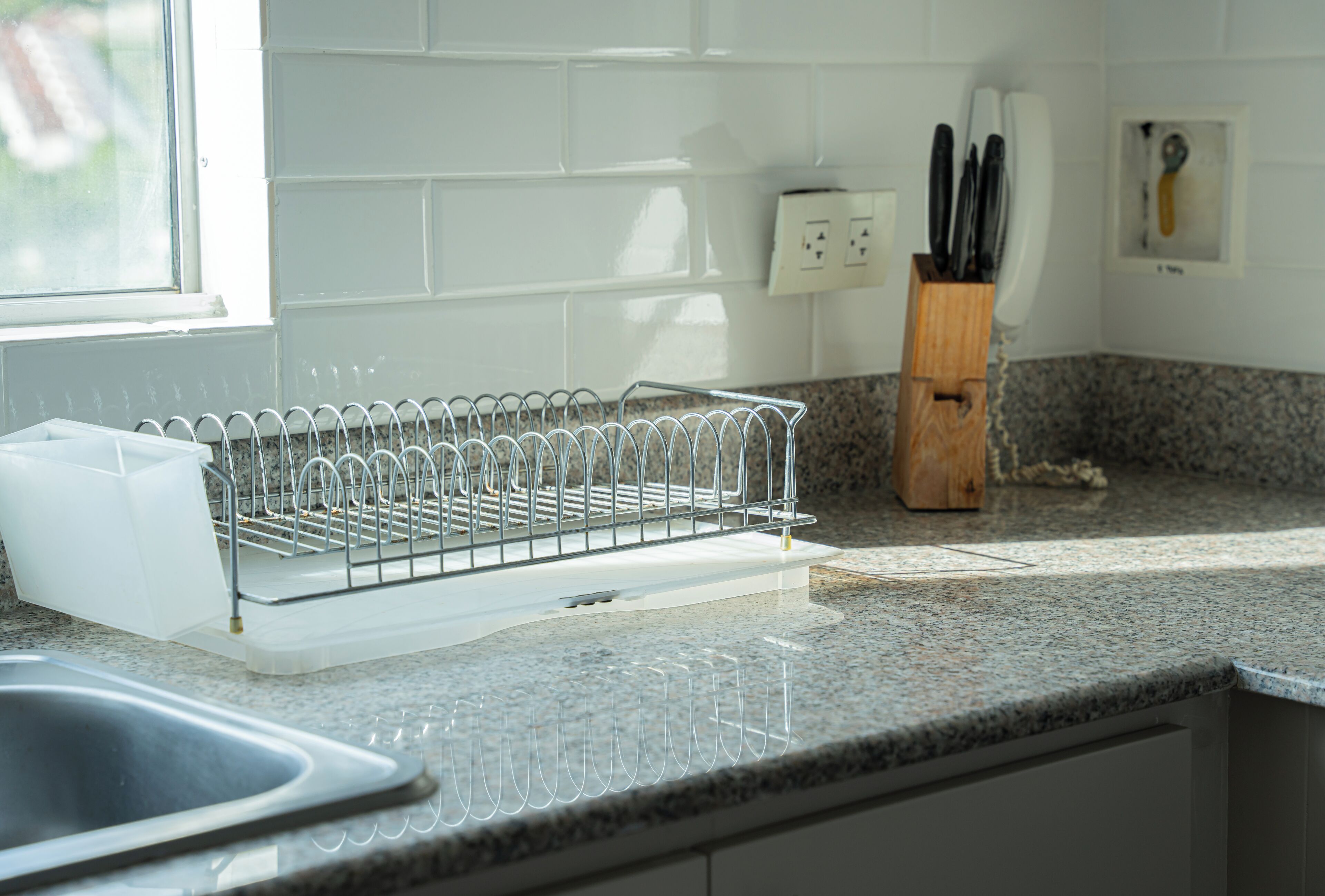 A kitchen with a dish rack, granite countertop, and a knife block.