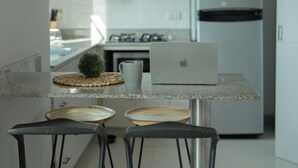Une cuisine moderne avec un plan de travail en granit, un ordinateur portable, une petite plante en pot et deux tabourets de bar.