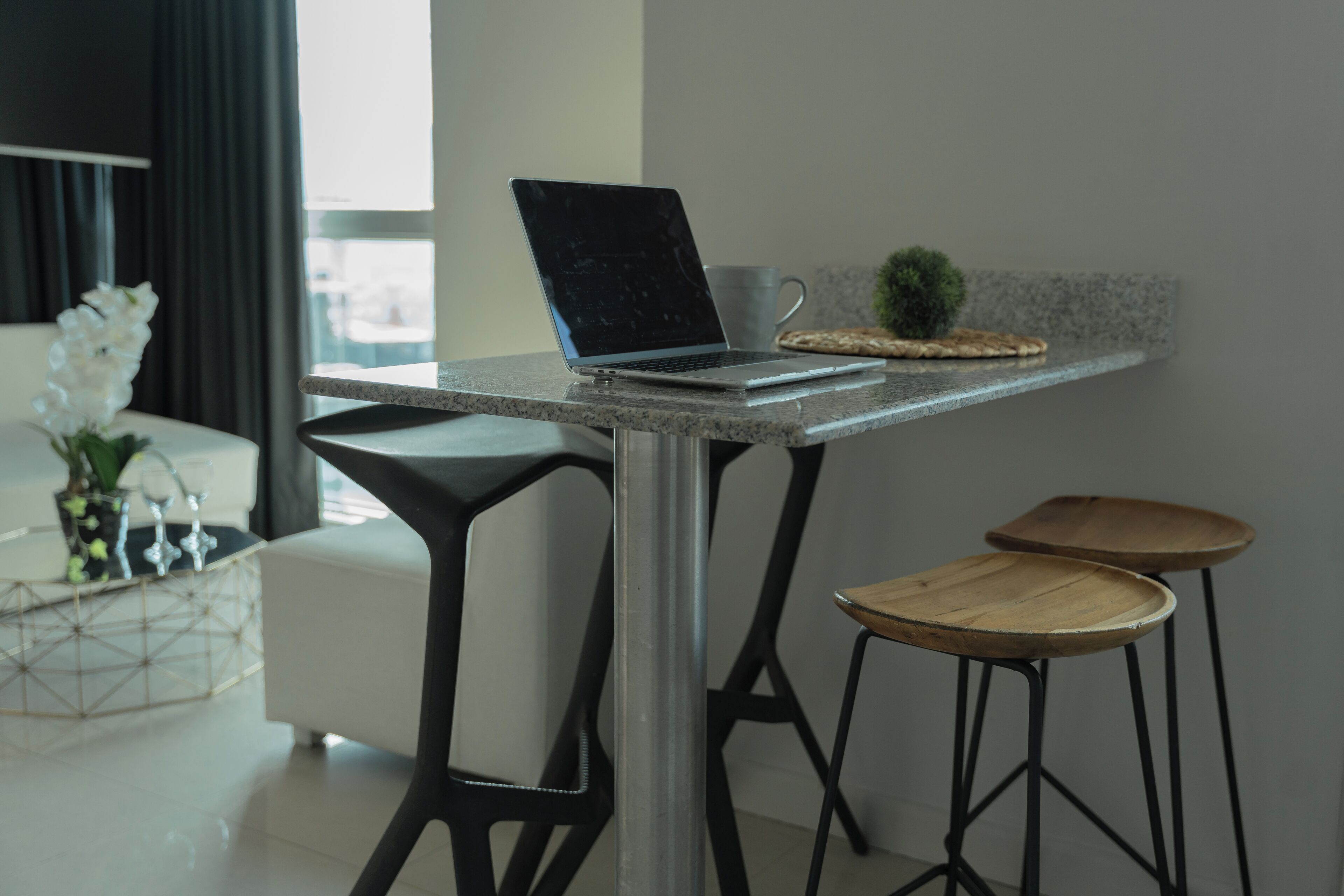 A modern kitchen with a laptop on a marble countertop, a coffee machine, and two stools.