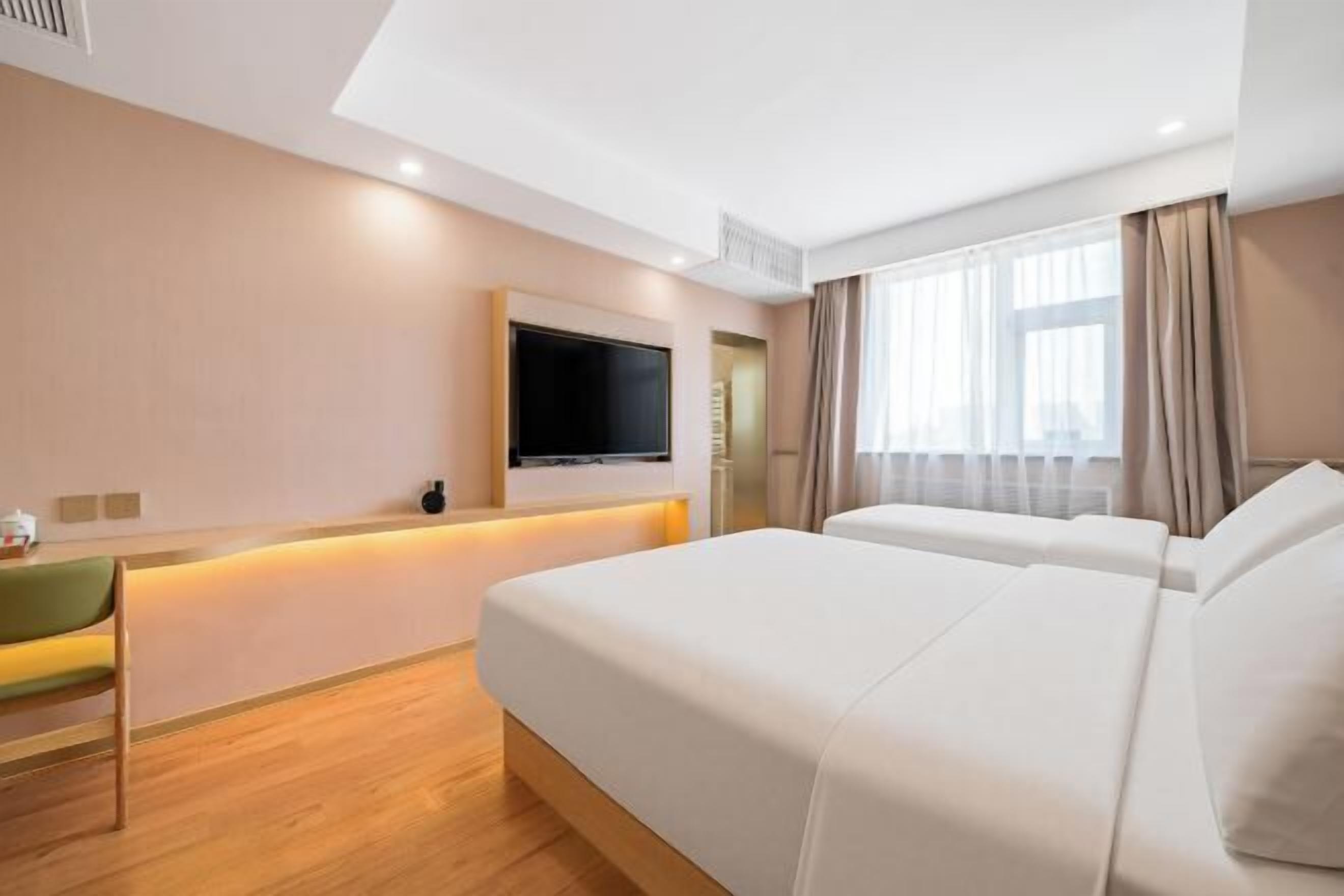 A hotel room with a bed, a desk, a chair, a TV, and a window with curtains.
