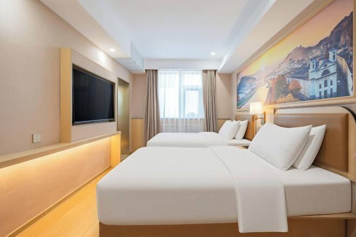 A hotel room with two beds, a flat-screen TV, a painting on the wall, and a window with curtains.