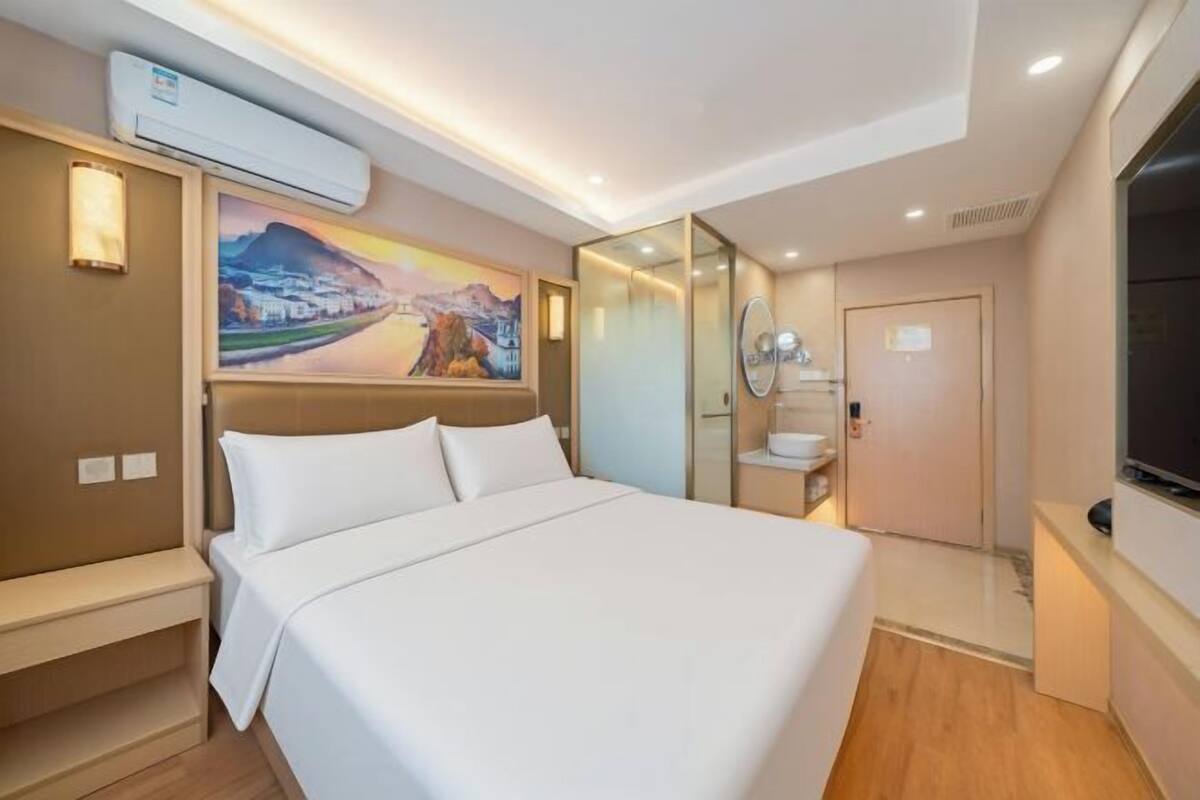 A hotel room with a bed, a painting, a TV, and a bathroom with a mirror.