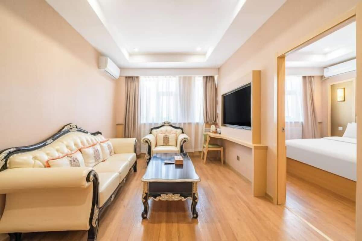 A hotel room with a sofa, armchair, coffee table, TV, and a bed.