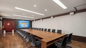 A conference room with a long wooden table, black chairs, recessed ceiling lights, and a projection screen. - Vienna Hotel (Beijing Wukesong Dacheng Road) (Beijing)