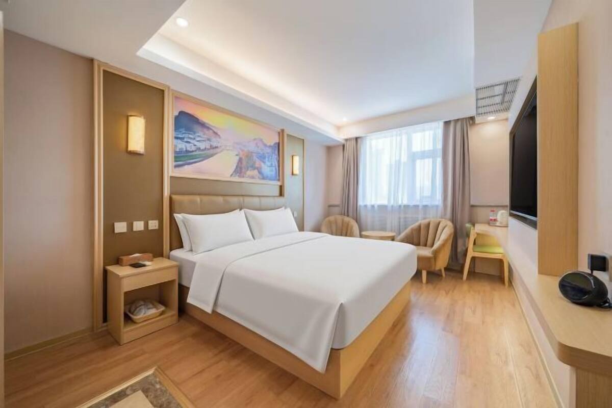 A modern hotel room with a large bed, a desk, a chair, a TV, and a painting on the wall.