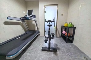 Un espace dédié à la remise en forme, équipé d’un tapis de course, d’un vélo elliptique et de poids.