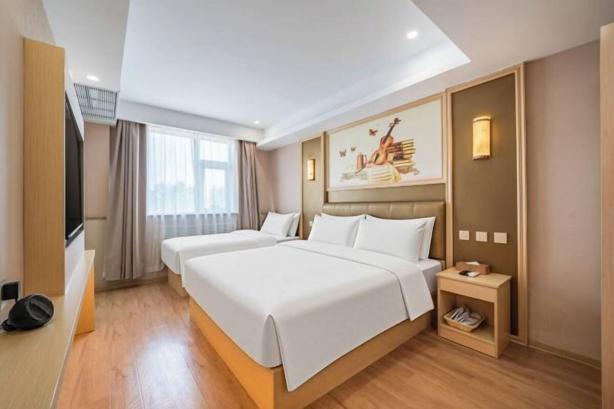 A hotel room with two beds, a TV, a painting, and a bedside table with a lamp.