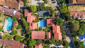 Eine Vogelperspektive zeigt einen luxuriösen Urlaubsort mit mehreren Schwimmbecken, Gebäuden mit roten Dächern und üppiger Vegetation.
