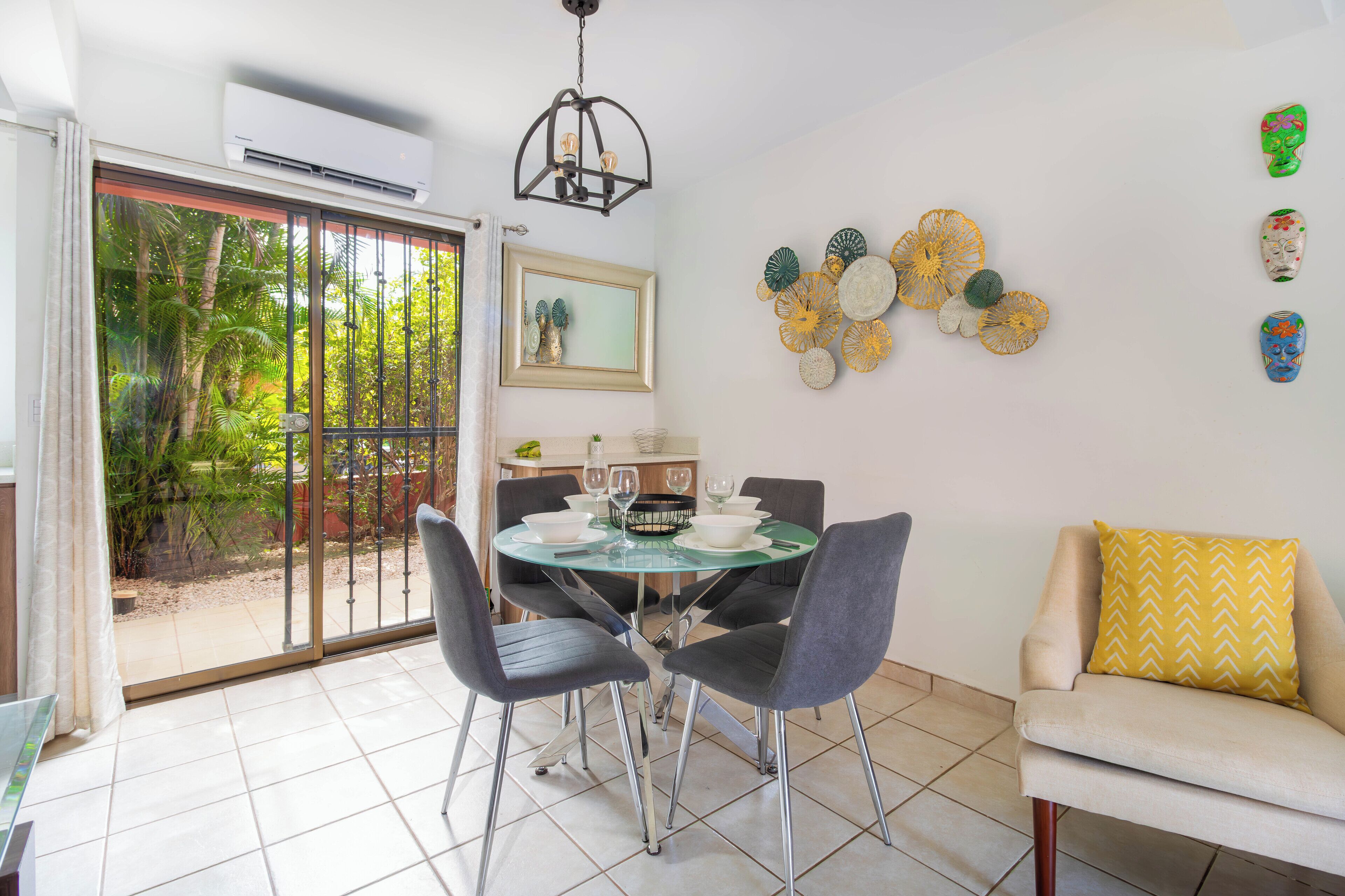 Un coin repas comprenant une table en verre, quatre chaises, un canapé agrémenté d’un coussin à motifs et un mur décoré d’assiettes.
