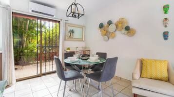 Un coin repas comprenant une table en verre, quatre chaises, un canapé agrémenté d’un coussin à motifs et un mur décoré d’assiettes.