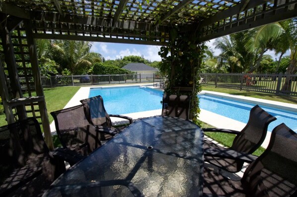 Relax by the pool in a shaded area surrounded by lush greenery and a palm tree.