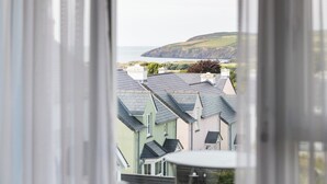 Vista attraverso una finestra su una zona residenziale costiera, con case e un paesaggio collinare sullo sfondo.