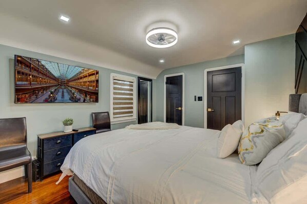 A modern bedroom with a large bed, a nightstand, a desk, and a wall-mounted TV.