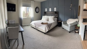 Une chambre à coucher comprenant un lit, une table de chevet, une chaise, un téléviseur et une fenêtre avec des rideaux.