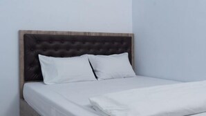 A bed with a tufted headboard, white bedding, and a wooden frame. - Hotel Padma Tangerang (Karawaci)