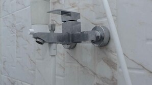 A bathroom with a wall-mounted shower faucet and a white marble wall. - Hotel Padma Tangerang (Karawaci)
