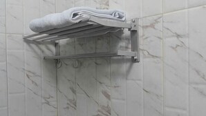 A bathroom with a towel rack holding folded towels, a shower area, and a marble tiled wall. - Hotel Padma Tangerang (Karawaci)