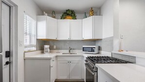 Una cocina funcional con armarios blancos, un microondas, una estufa a gas y un lavamanos.
