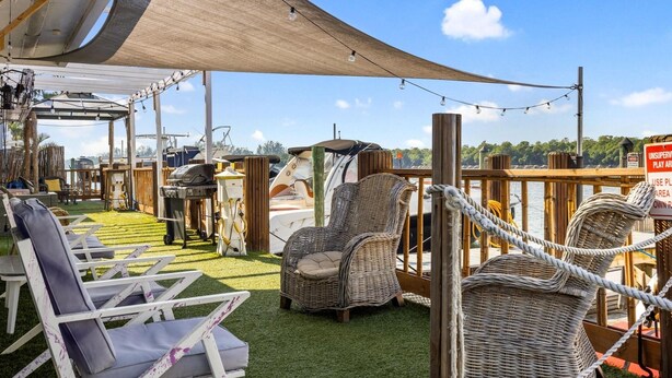 Una terraza con sillas de mimbre y una zona de parrilla, con vista a un cuerpo de agua.