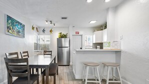 Una cocina moderna con un refrigerador de acero inoxidable, taburetes de bar blancos y una pequeña isla.