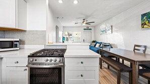 Una cocina moderna con estufa a gas, horno y microondas. Hay una zona de comedor con mesa y sillas, y un sofá azul al fondo.