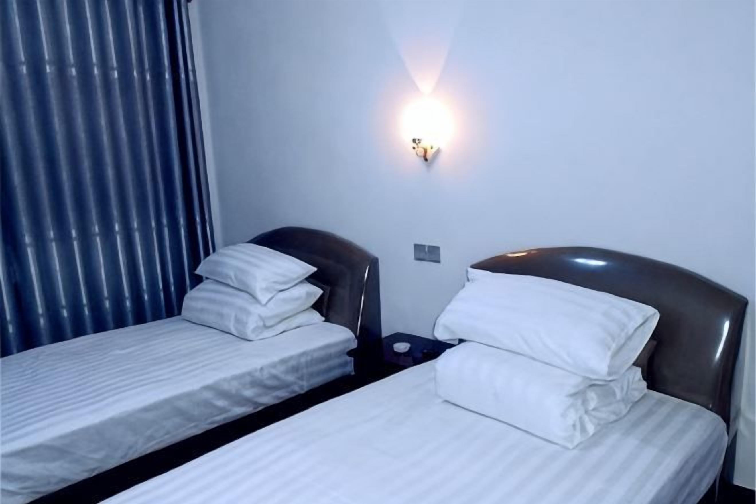 Two single beds with headboards, a wall-mounted light, and a window with blinds.