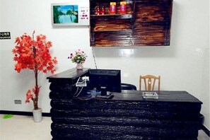 A reception desk with a potted plant, a chair, and a wall-mounted shelf with items. - Longwangshan Huanle Inn (Anji)