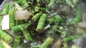 Una olla con agua hirviendo, verduras verdes y algas.