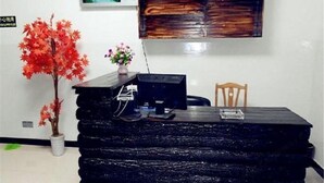 Un mostrador de recepción con una computadora, una planta en maceta y una silla de madera.